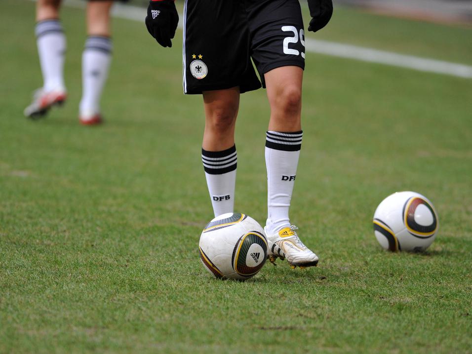 Nahaufnahme eines Fußballspielers mit einem Ball auf dem Rasen, im Hintergrund ein weiterer Ball.