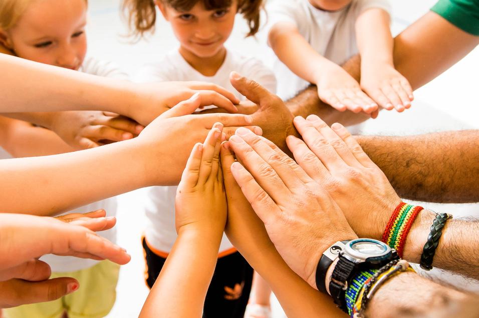 Kinder und Erwachsene legen ihre Hände in einem Kreis zusammen, symbolisieren Zusammenarbeit und Gemeinschaft.